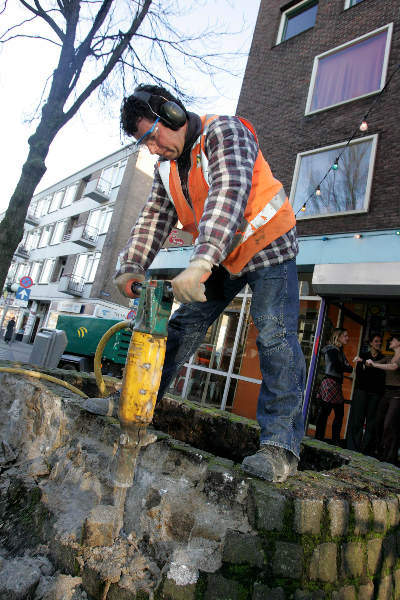 Verwijderen Bloembak voor de Plak met afbouwhamer Simone en Geertje en Michelle kijken toe