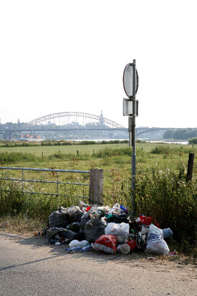 \"Vuilniszakken bij Waalstrand met brug op achtergrond\"