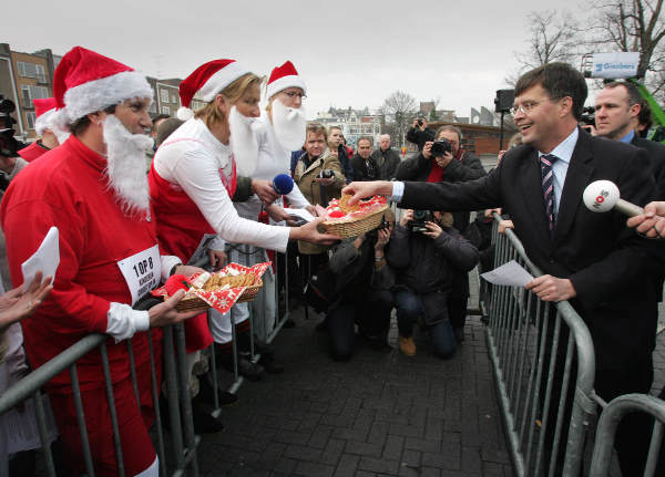 \"J.P Balkenende neemt een koekje aan van aktievoerders bij de onthulling van de godenpijler in Nijmegen\"