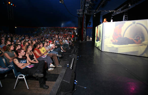 \"Lowlands, Biddinghuizen. Wetenschapper Peter Hagoort van de RU houdt een lezing over hersenprocessen en heeft een live-verbinding met de CT-scanner in Nijmegen. Gezichten in de zaal gefilmd laten hersenactiviteit zien bij de proefperoon in Nijmegen._\"