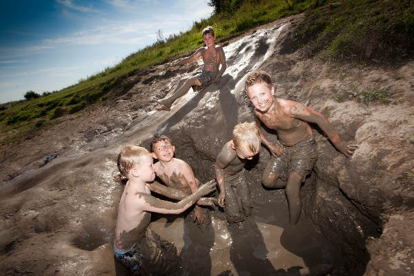 \"Ooij, Bisonbaai, oudere kinderen spelen in de modder op een modderglijbaan\"